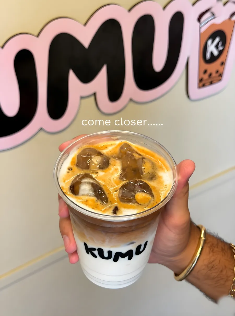 Mano sosteniendo un café helado de Kumu frente al logo